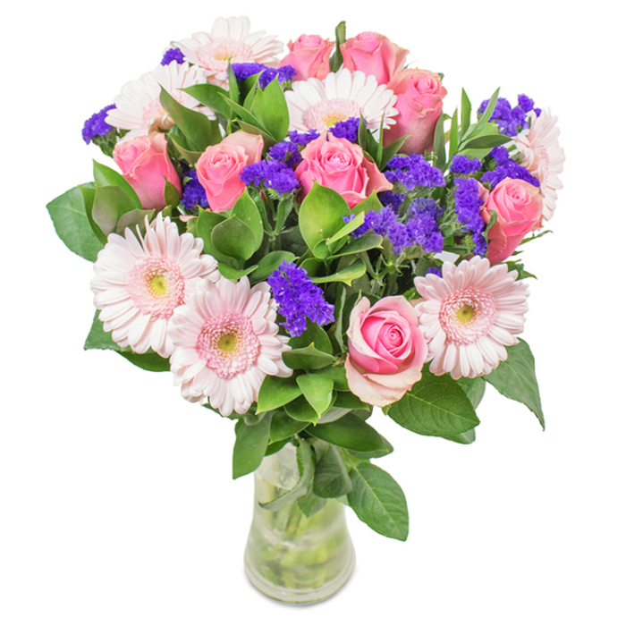 In a clear, elegant glass vase set against a crisp white background, this striking bouquet captures the refined artistry that defines Stamford Hill's floral tradition. Approximately seven to nine perfectly spiralled pink roses, their petals tightly wrapped or unfurling in delicate gradients from soft blush to rich rose, form the heart of the arrangement. Intertwined among them, five to seven large-headed gerbera daisies shine with pale pink hues and subtle, nearly white centres, creating an irresistible focal point. Scattered throughout the bouquet, clusters of vivid purple statice or limonium introduce a lively textural dimension and a dynamic pop of colour, much like the eclectic vibrancy found among Stamford Hill's local shops and bakeries. The lush, deep green foliage grounds the composition with freshness and a hint of woodland scent, with stems and crystal-clear water visible through the vase-an invitation to admire the bouquet's natural longevity. Assembled by expert florists familiar with Stamford Hill's tastes, this arrangement is ideal for birthdays, anniversaries, Mother's Day, or brightening a home or office in N16. It radiates celebration and affection, a tribute to meticulous care and the neighbourhood's diverse beauty.